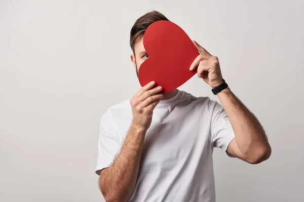 Mann versteckt Gesicht hinter leerem Papier geschnitten Herzkarte isoliert auf grau — Stockfoto