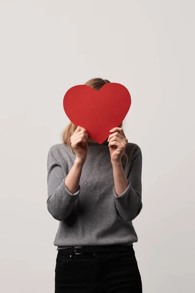 Young woman hiding face behind empty red paper cut heart card isolated on grey — Stock Photo