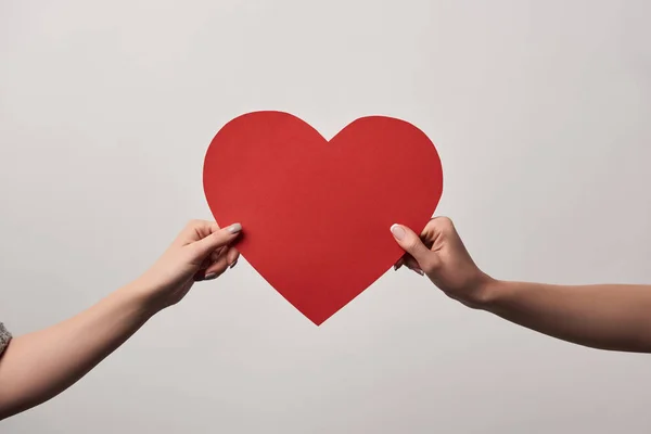 Recortado vista de niñas sosteniendo juntos en blanco tarjeta del corazón aislado en gris - foto de stock