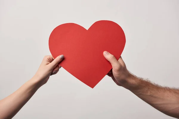 Vista parcial de la pareja que mantiene unida la tarjeta de corazón en blanco aislada en gris - foto de stock