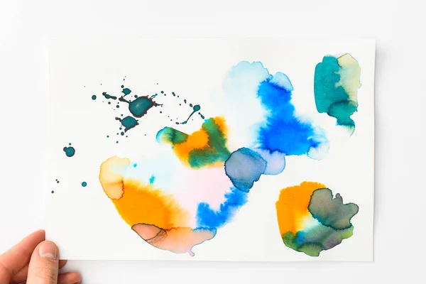 Mann hält Papier mit abstrakten Aquarellfarben blau, gold und gelb auf weißem Hintergrund — Stockfoto