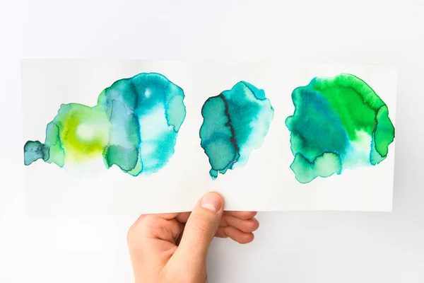 Homme tenant du papier avec aquarelle abstraite bleu et vert déversements sur fond blanc — Photo de stock