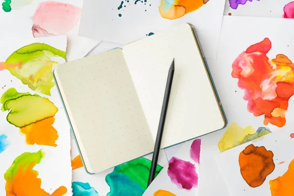 Top view of white notebook with pencil on background with abstract watercolor paintings — Stock Photo