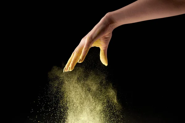 Cropped view of woman dropping yellow holi powder on black background — Stock Photo