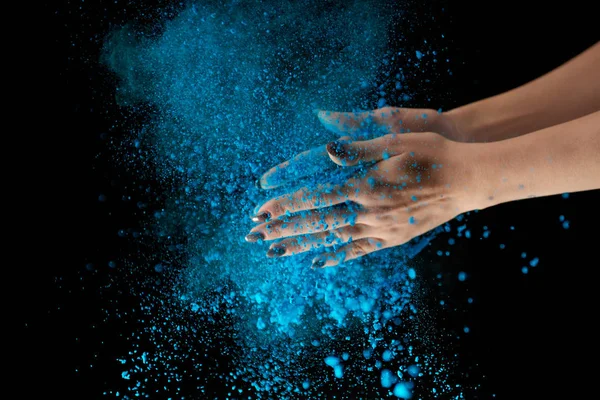 Abgeschnittene Ansicht einer erwachsenen Frau, die blaues Holi-Puder in der Hand hält und auf schwarzem Hintergrund klatscht — Stockfoto