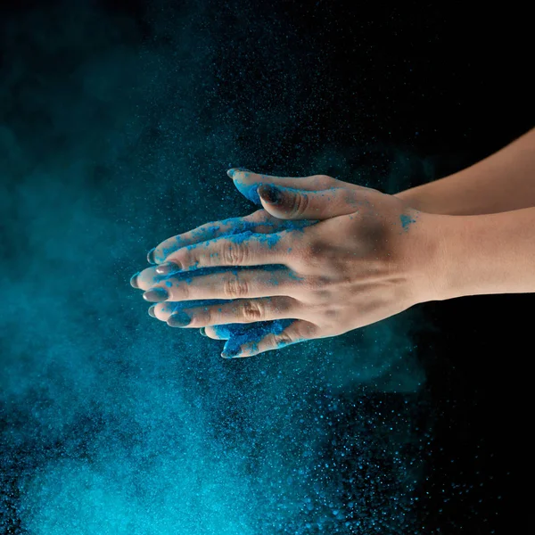 Abgeschnittene Ansicht einer erwachsenen Frau, die blaues Holi-Puder in der Hand hält und auf schwarzem Hintergrund klatscht — Stockfoto