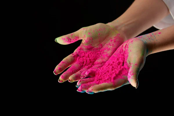 Vue recadrée de la femme adulte avec poudre holi rose sur les mains isolées sur noir — Photo de stock