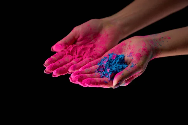 Vista recortada de adulto con las manos en polvo rosa sosteniendo polvo holi azul aislado en negro - foto de stock