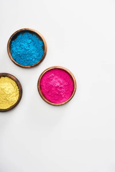 Vue du dessus des bols en bois avec poudre holi rose, bleu et jaune sur fond blanc — Photo de stock