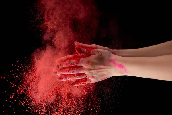 Vista recortada de la mujer adulta sosteniendo polvo de holi rojo y aplaudiendo sobre fondo negro - foto de stock