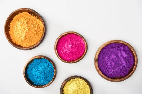 Top view of wooden bowls with pink, blue, yellow, purple and orange holi powder on white background — Stock Photo