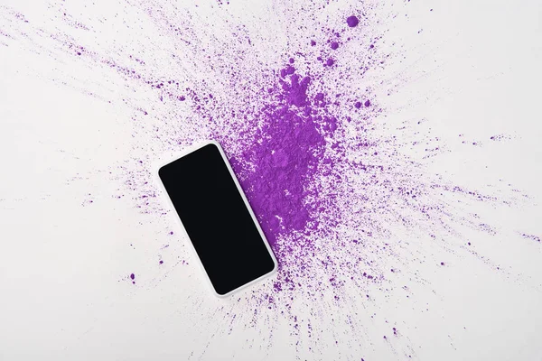 Ansicht des Smartphones von oben mit leerem Bildschirm und Explosion von lila Holi-Pulver auf weißem Hintergrund — Stockfoto