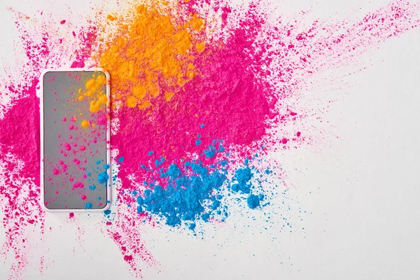 Vista superior del teléfono inteligente y explosión de polvo de holi multicolor sobre fondo blanco - foto de stock
