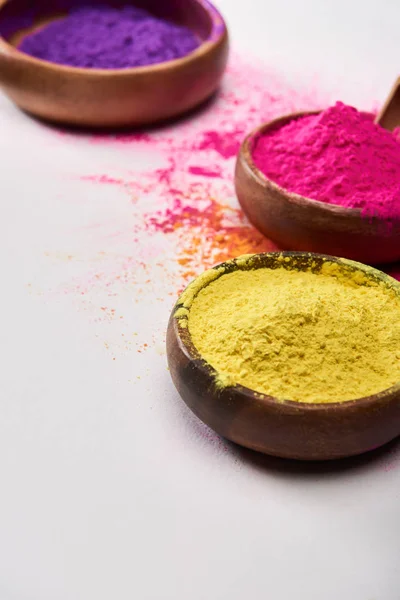 Wooden bowls with yellow, pink and purple holi powder on white background — Stock Photo