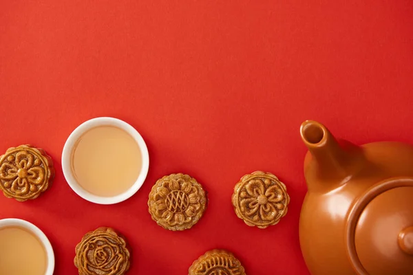 Vue de dessus des mooncakes traditionnels, théière et tasses isolées sur rouge — Photo de stock