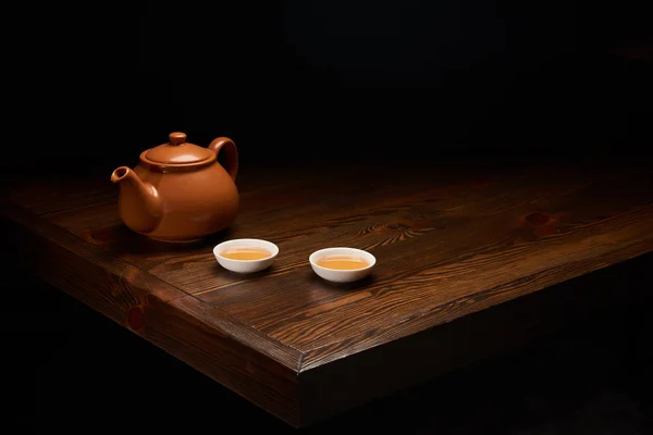 Olla con té tradicional chino y tazas en mesa de madera aislada en negro - foto de stock
