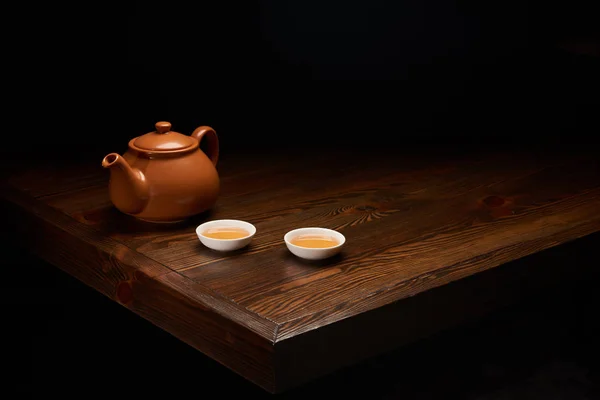 Pot with traditional chinese tea and cups on wooden table isolated on black — Stock Photo