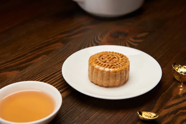 Selective focus of mooncake with tea cup and gold ingots on wooden table — Stock Photo