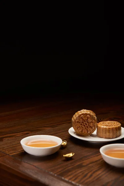 Traditional mooncakes with tea cups and gold ingots isolated on black with copy space — Stock Photo