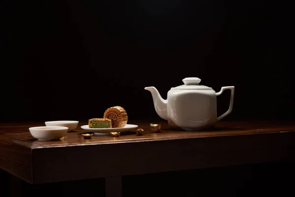 Gâteaux chinois traditionnels, théière et lingots d'or sur table en bois isolé sur noir avec espace de copie — Photo de stock