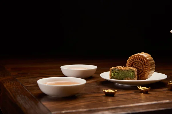 Gâteaux chinois traditionnels, tasses de thé et lingots d'or isolés sur noir — Photo de stock