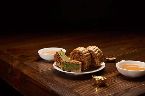 Traditional chinese mooncakes, cups of tea and gold ingots isolated on black — Stock Photo