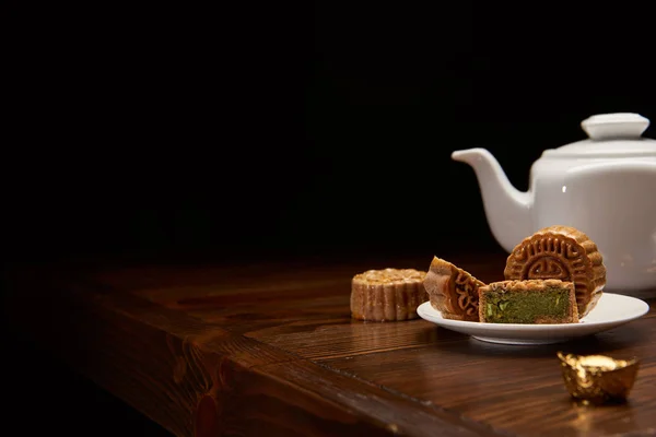 Traditional chinese mooncakes, tea pot and gold ingot on wooden table isolated on black with copy space — Stock Photo