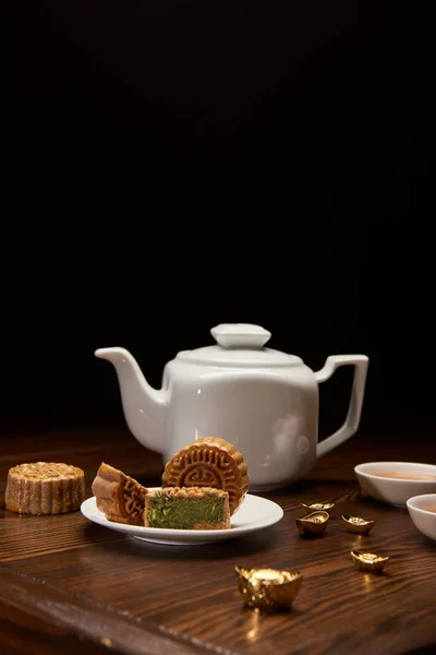 Традиційні китайські місячні млинці, чайний горщик і золоті злитки на дерев'яному столі ізольовані на чорному — стокове фото
