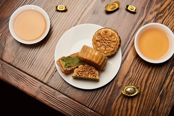 Традиционные лунные пирожные с чашками чая и золотыми слитками на деревянном столе — стоковое фото