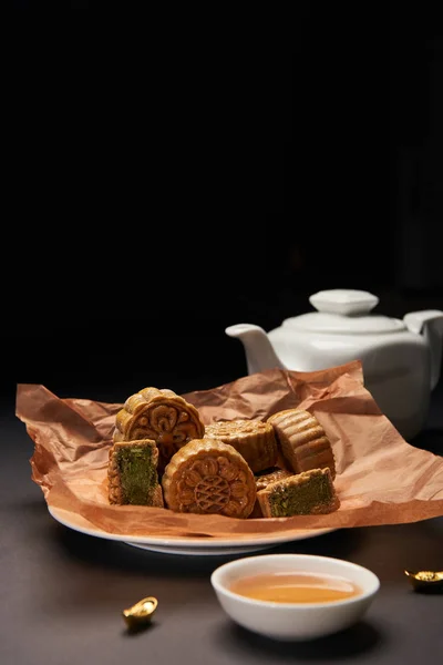 Selective focus of traditional chinese mooncakes, tea pot and gold ingots on wooden table isolated on black — Stock Photo