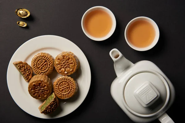 Vista superior de tartas de luna, tazas y tetera aislados en negro - foto de stock