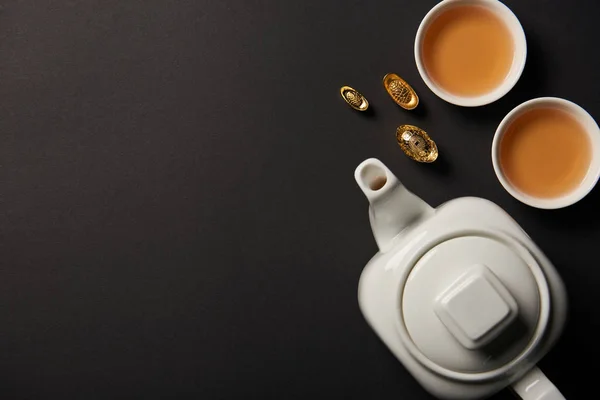 Top view of gold ingots, tea pot and cups isolated on black with copy space — Stock Photo