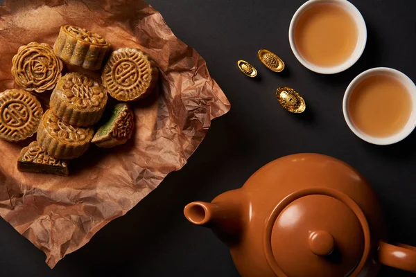 Top view of mooncakes, tea pot and gold ingots isolated on black — Stock Photo