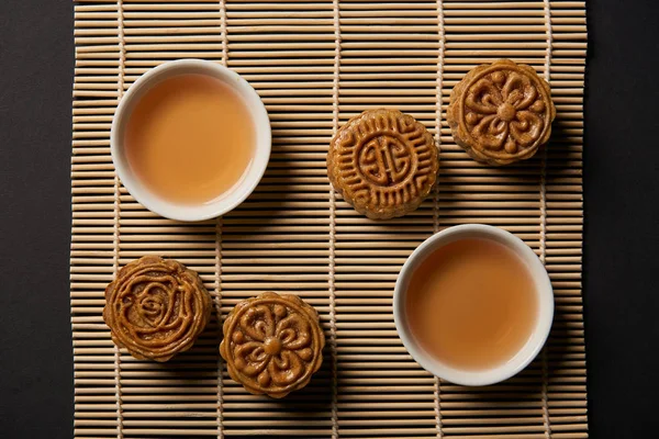 Vista superior de los tradicionales pasteles de luna y tazas de té en la estera de mesa de bambú - foto de stock