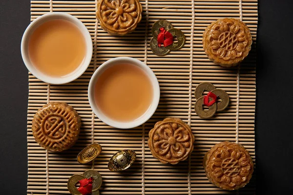 Top view of mooncakes, feng shui coins and tea pot with cups on bamboo table mat — Stock Photo