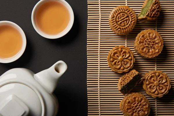 Vue de dessus des mooncakes traditionnels, théière et tasses sur le tapis de table en bambou — Photo de stock