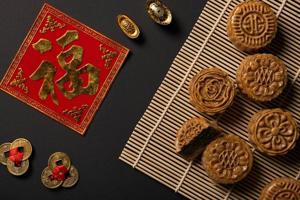 Vue de dessus des mooncakes traditionnels avec talismans chinois et tapis de table en bambou isolé sur noir — Photo de stock