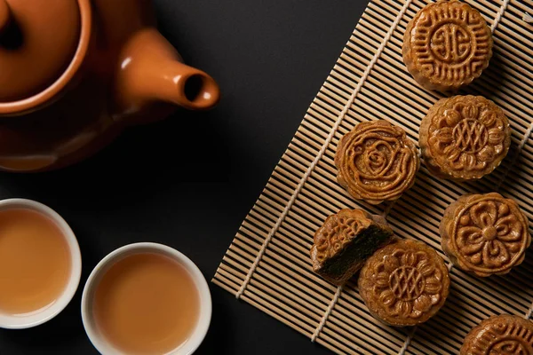 Vista superior de tortas de luna tradicionales, tetera y tazas en la estera de mesa de bambú - foto de stock