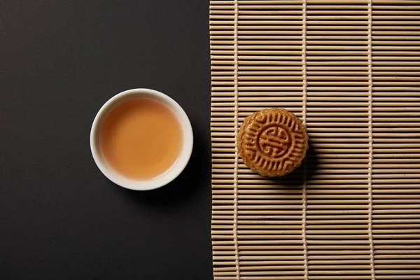 Vista superior del pastel de luna y la taza de té en la estera de mesa de bambú - foto de stock