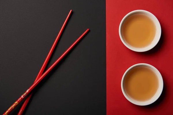 Vue de dessus des baguettes avec du thé chinois traditionnel sur fond rouge et noir — Photo de stock
