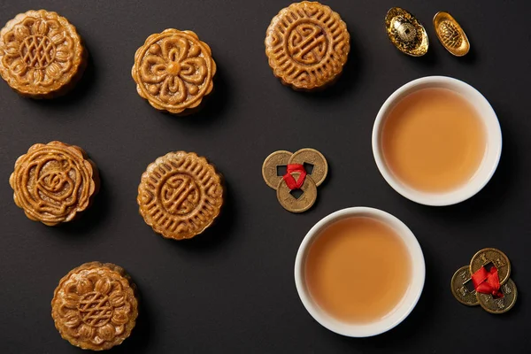 Vista superior de las tradicionales tartas de luna, tazas de té y monedas de feng shui aisladas en negro - foto de stock