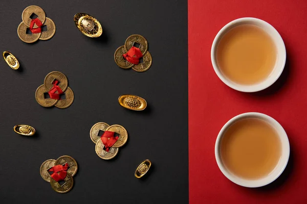 Top view of tea cups and feng shui coins on red and black background — Stock Photo