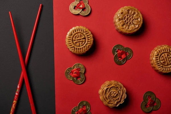 Top view of mooncakes, feng shui coins and chopsticks on red and black background — Stock Photo