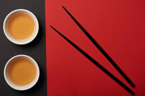 Верхний вид чашки чая и палочки для еды на красном и черном фоне — стоковое фото