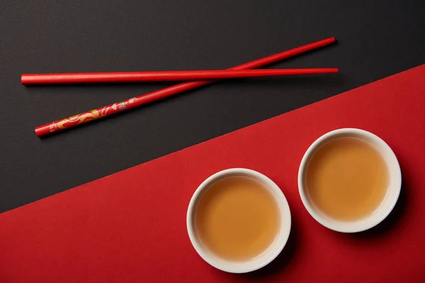 Vue de dessus des baguettes avec du thé chinois traditionnel sur fond rouge et noir — Photo de stock