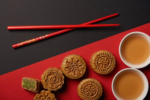 Vista superior de las tradicionales tartas de luna chinas con palillos sobre fondo rojo y negro - foto de stock