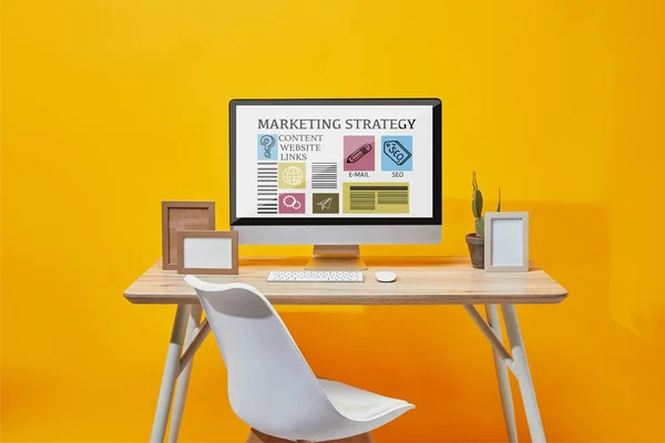 Ordenador con estrategia de marketing sitio web en la pantalla en la mesa de madera sobre fondo amarillo - foto de stock