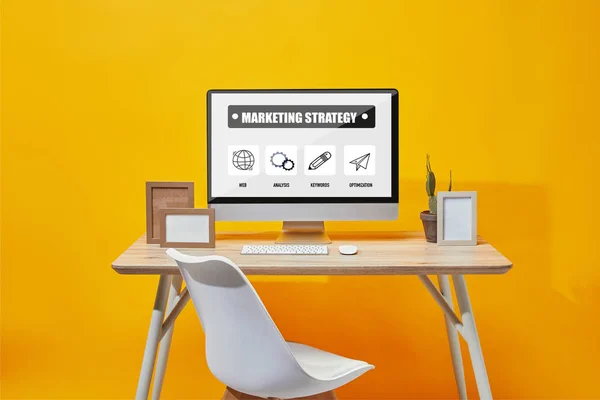 Комп'ютер з маркетинговою стратегією на екрані за дерев'яним столом на жовтому фоні — стокове фото