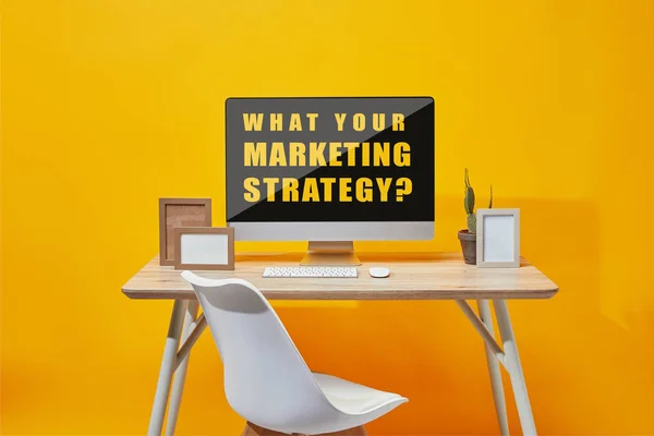 Computador com o que sua estratégia de marketing pergunta na tela na mesa de madeira no fundo amarelo — Fotografia de Stock