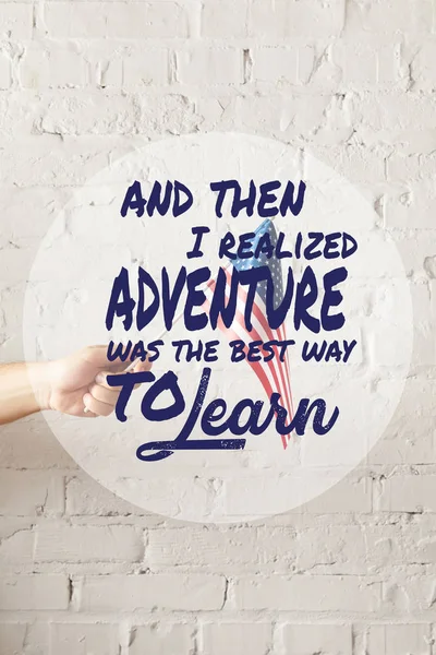 Cropped image of man holding american flagpole against white brick wall with and then i realized adventure was the best way to learn quote — Stock Photo